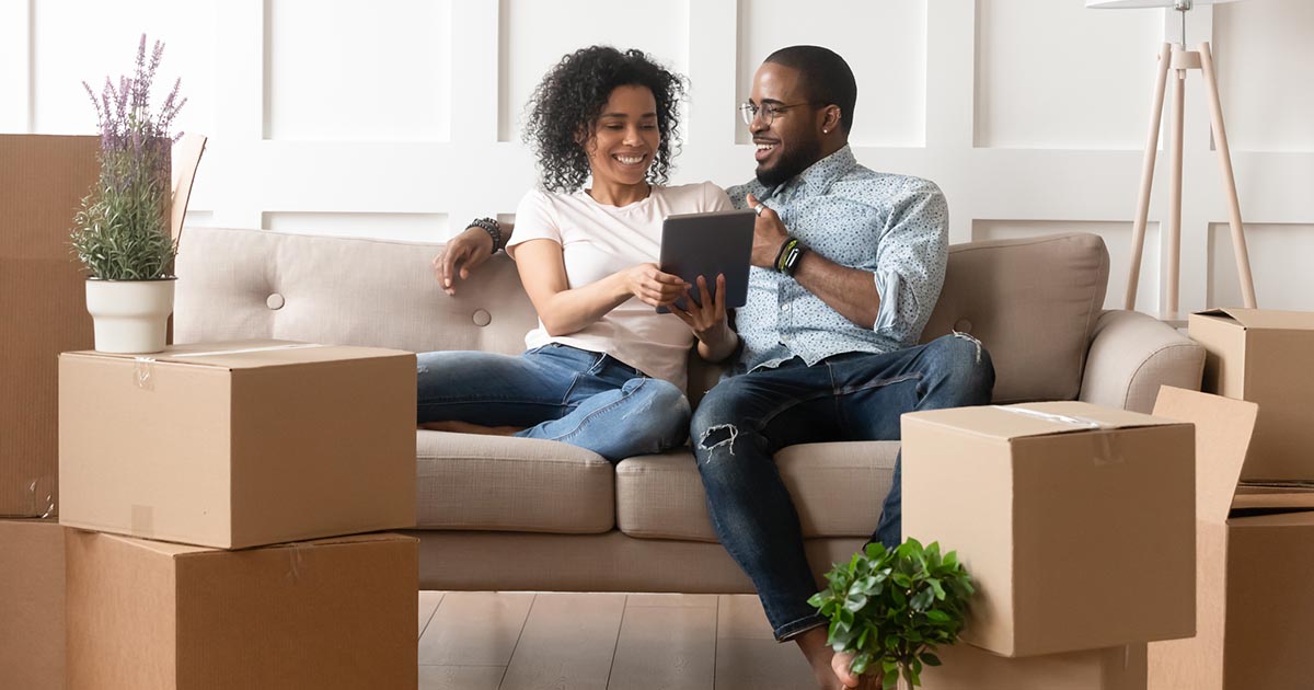 young couple recently moved into a new home sitting on the couch looking at a tablet